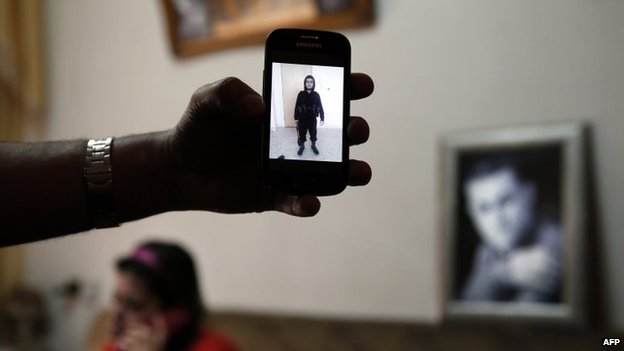 The brother of Mohammed Musallam holds a phone showing a photograph of him dressed in black, military fatigues in Syria